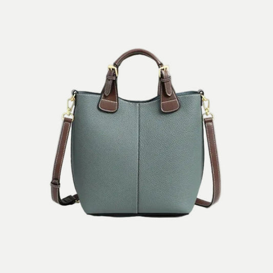 Green handbag with brown straps and handle on a light gray background